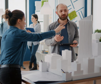 Team of coworkers analyzing maquette and building model to plan construction on tablet