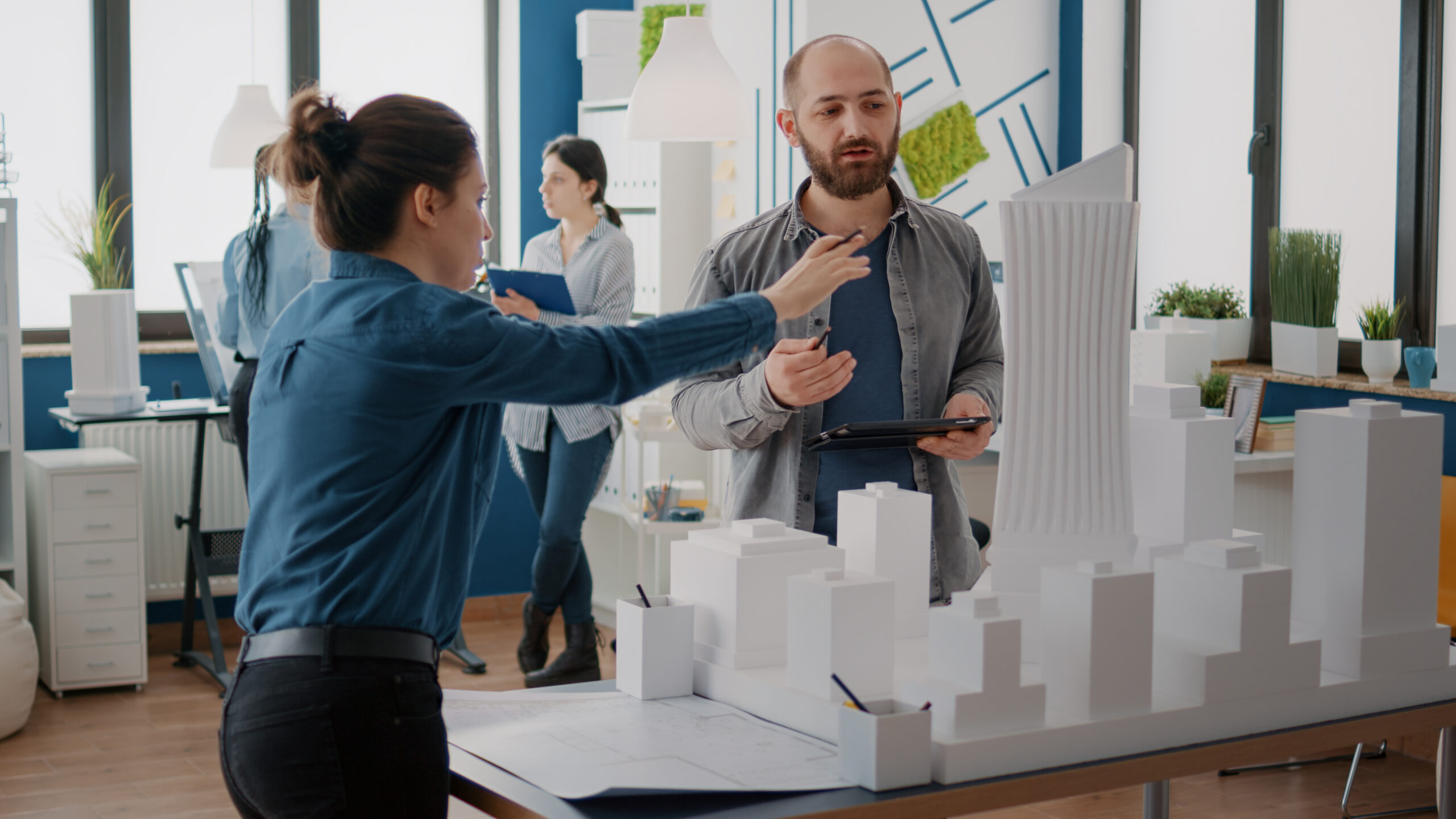 Team of coworkers analyzing maquette and building model to plan construction on tablet